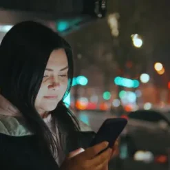 دانلود فوتیج دختر در حال چک کردن گوشی در یک شب بارانی